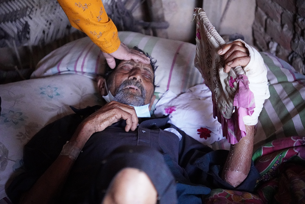 A hand touches the forehead of a man lying in bed