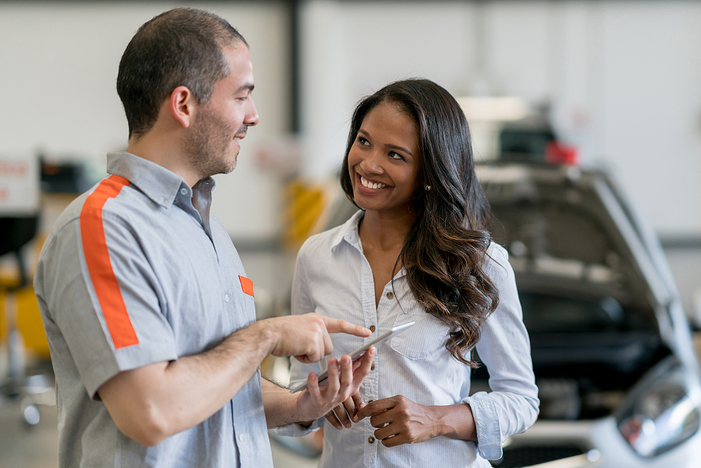Happy woman taking her broken car to the mechanic at an auto repair shop
