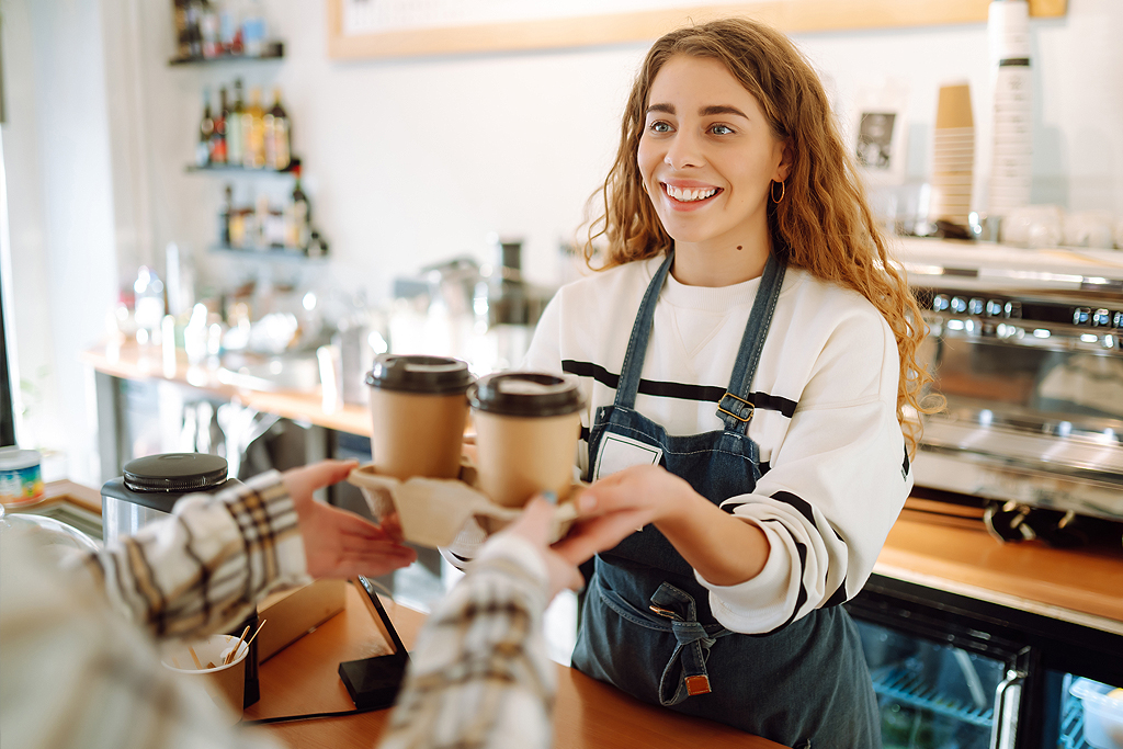 Smiling barista- girl giving take away coffee cups to a customers.